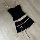 Black two-piece outfit with pink straps and belt on a wooden floor